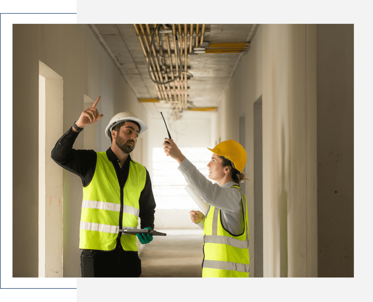 Two construction workers inspecting ceiling pipes.